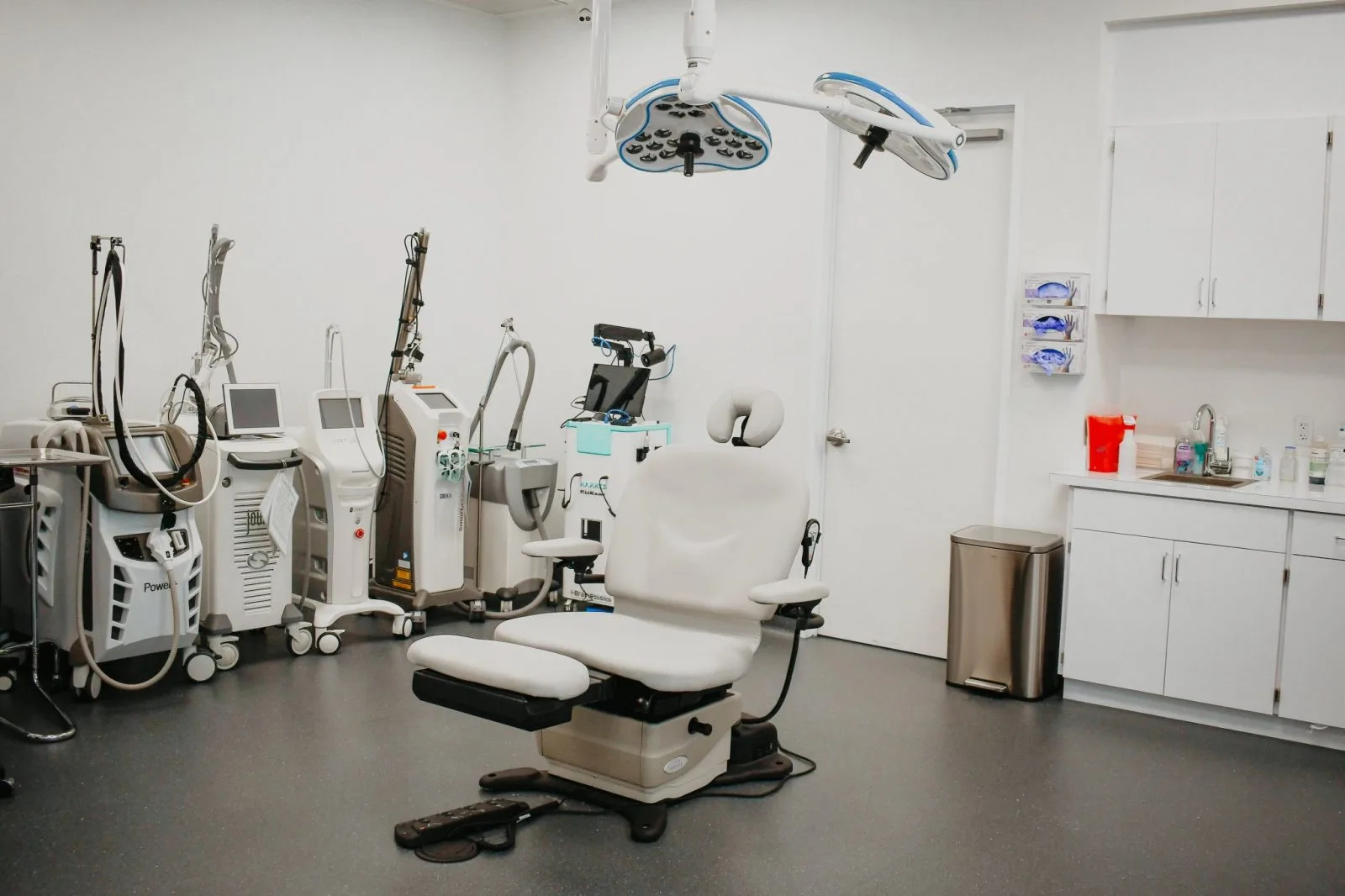 Dermatology treatment room with surgical lights, examination chair, and laser and injection devices